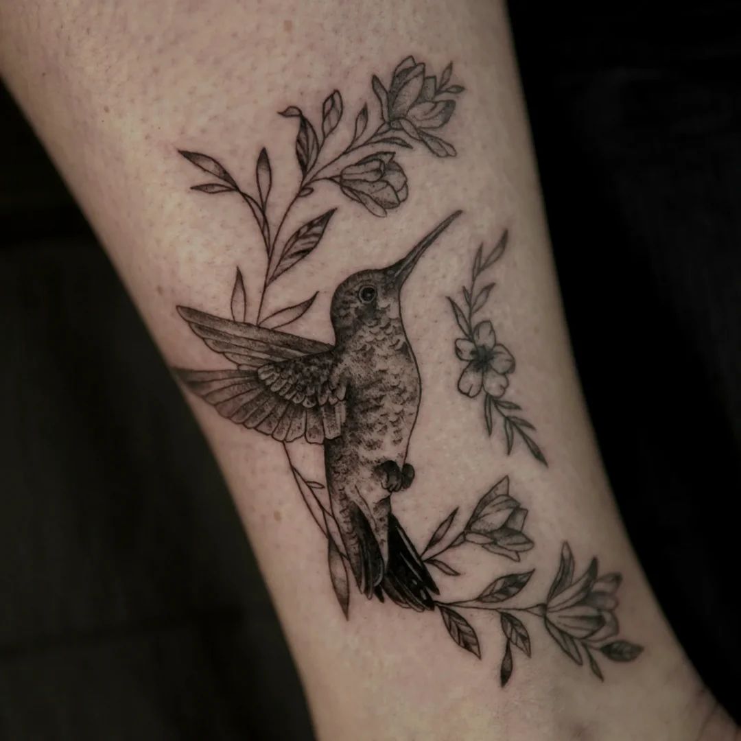 Tatuaże damskie: koliber z roślinnym motywem na przedramieniu